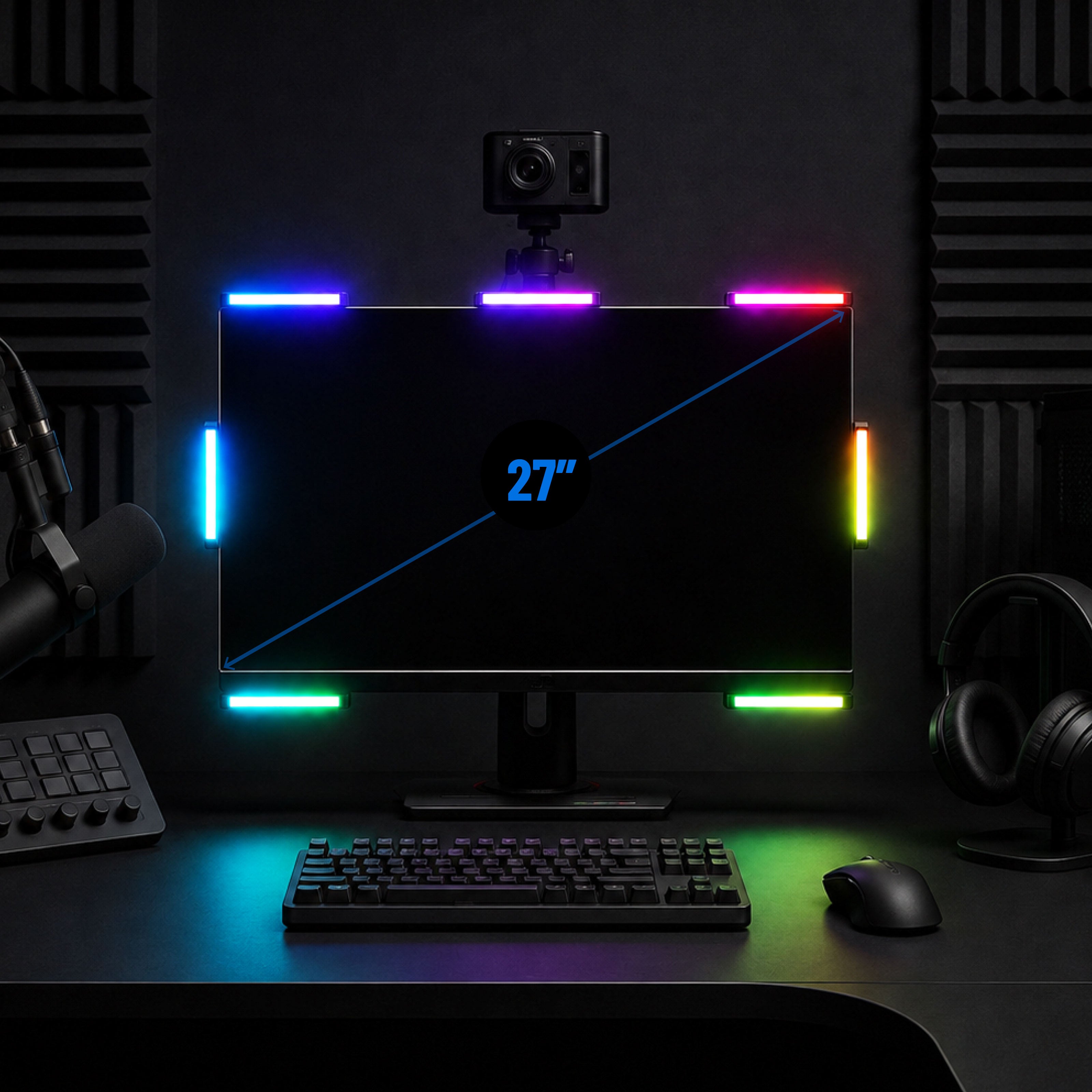 A 27-inch monitor on a desk with colorful LED strip lights around the edges, a webcam mounted above, headphones, keyboard, mouse, and microphone in a dark studio setup.