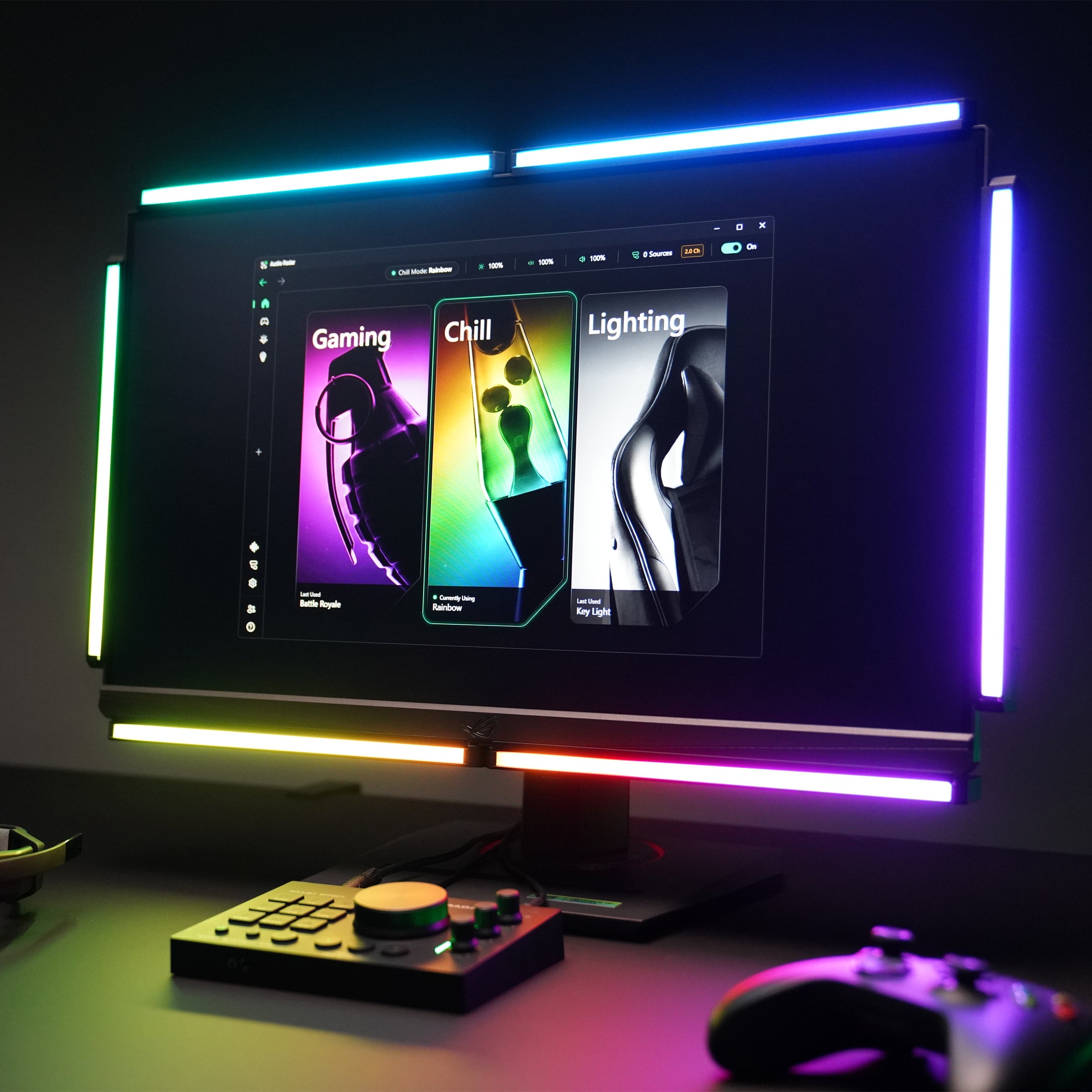 A desktop monitor setup in a dark room with RGB LED light bars around the screen, displaying colorful gaming-themed content. A game controller and a small control pad sit on the desk in front.